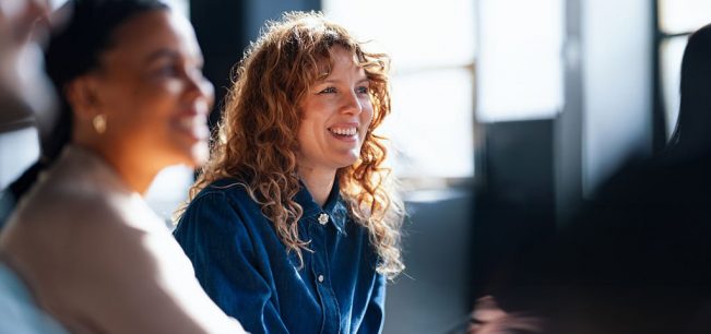 Two cheerful coworkers share ideas in a vibrant office setting, fostering a positive and collaborative workplace atmosphere.